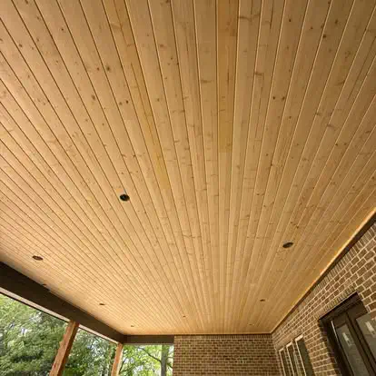 A tongue and groove wood porch ceiling with recessed lights over a covered patio