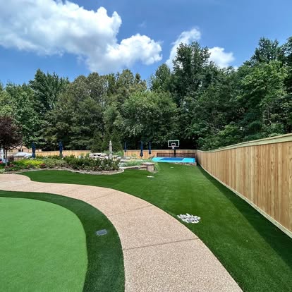 A long privacy fence around a turf lawn and sports court